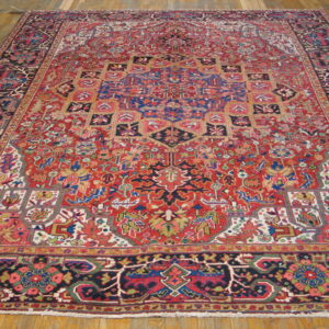 Traditional red rug featuring intricate blue, green, and cream geometric designs on wooden flooring.