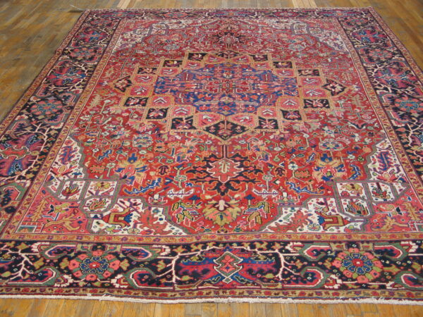 Large red and navy blue oriental rug with a complex central medallion pattern on light wood plank flooring.