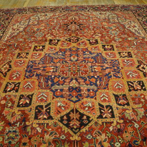 Traditional red rug with complex navy and gold medallions and geometric squares covering light wood floors.