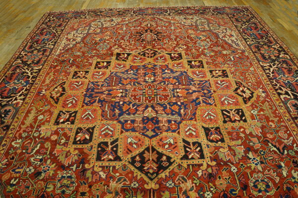 Traditional red rug with complex navy and gold medallions and geometric squares covering light wood floors.