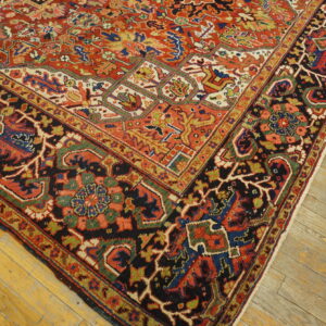 A detailed rug featuring red, black, blue, and gold geometric motifs on distressed light wood planks.
