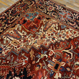 Ornate traditional rug featuring dense red, cream, and blue geometric patterns on wood flooring.