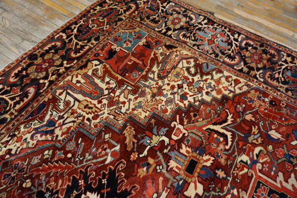 Ornate traditional rug featuring dense red, cream, and blue geometric patterns on wood flooring.