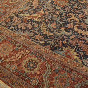 Low-pile traditional rug with navy and rust floral designs resting on light wood plank flooring.