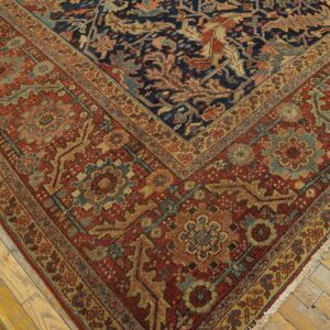 A dark navy and rust red patterned rug with gold and teal accents sits on distressed light wood floors.
