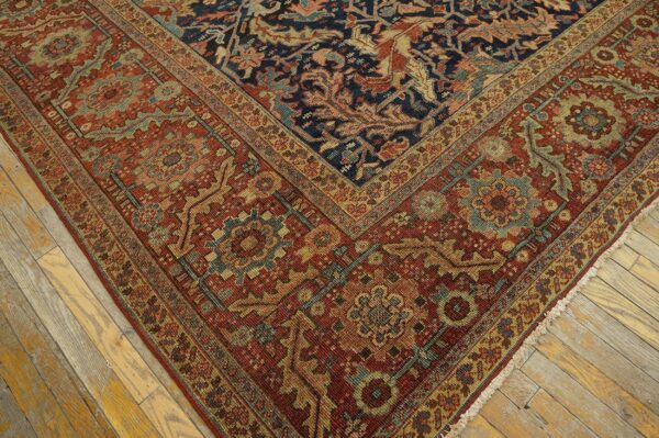 A dark navy and rust red patterned rug with gold and teal accents sits on distressed light wood floors.
