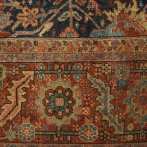 Close-up of a navy and rust traditional rug border detail resting on light wooden flooring.
