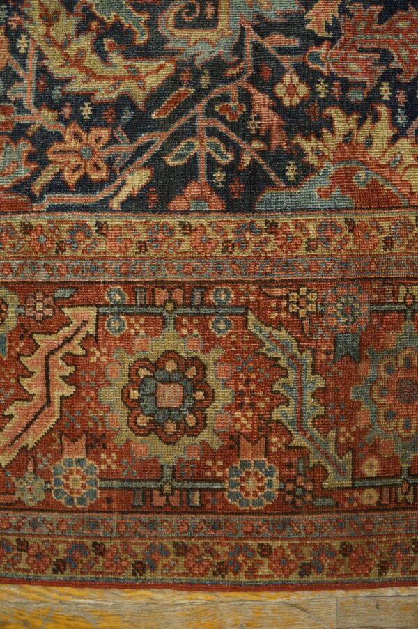 Close-up of a navy and rust traditional rug border detail resting on light wooden flooring.