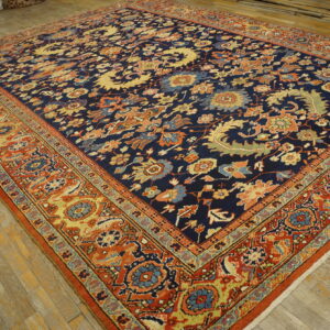 Ornate navy blue rug with a dense multi-color pattern and wide orange border rests on a wood floor.