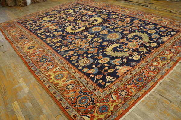 Ornate navy blue rug with a dense multi-color pattern and wide orange border rests on a wood floor.