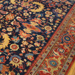 Navy blue rug with detailed red, yellow, and blue floral patterns lies on hardwood floor planks.