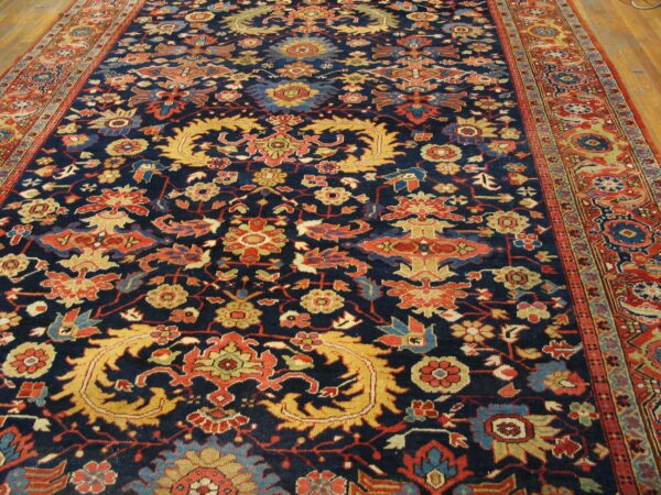 Traditional navy rug featuring ornate red, gold, and light blue botanical designs on wood floor.
