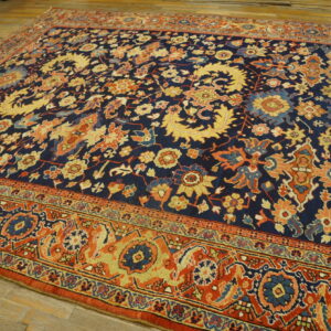 Intricate floral rug featuring a navy field, rust border, and colorful botanical details on light wood flooring.