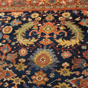 Detailed rug showing a navy blue field with complex floral patterns and an orange-red border.