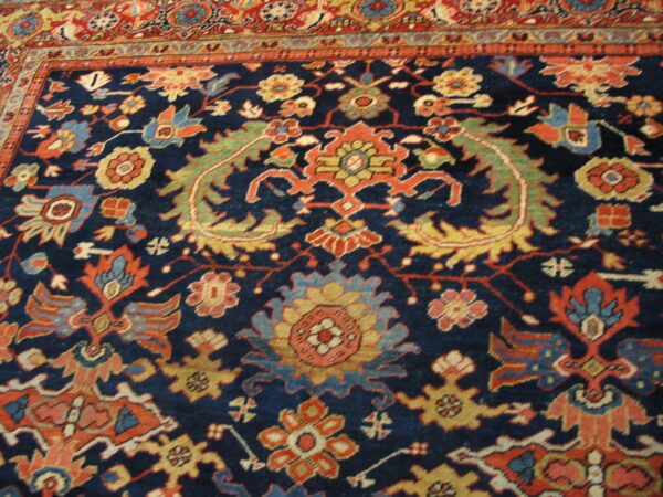 Detailed rug showing a navy blue field with complex floral patterns and an orange-red border.