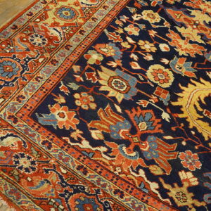Detailed view of a traditional navy rug with rust borders and ornate gold and blue patterns on wooden flooring.