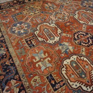 Low-pile rug in rusty red, navy, and cream geometric patterns rests on light wooden flooring.