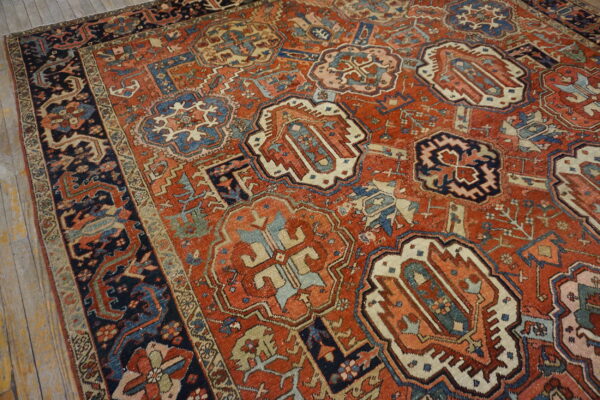 Low-pile rug in rusty red, navy, and cream geometric patterns rests on light wooden flooring.
