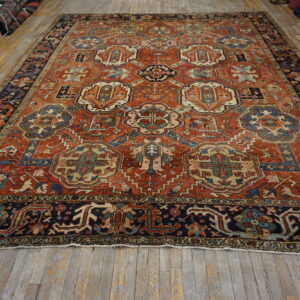 Ornate rust and navy rug with repeating stylized medallions lying on distressed hardwood floors.
