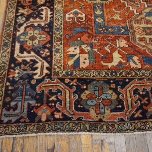 Rust-red field and navy blue border rug with a detailed geometric pattern on distressed wood planks.