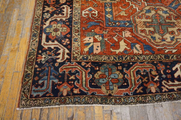 Rust-red field and navy blue border rug with a detailed geometric pattern on distressed wood planks.