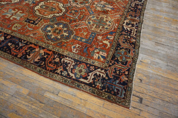 Rusty orange and navy traditional rug with detailed borders sits on heavily distressed, light wood flooring.
