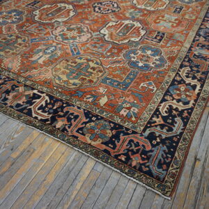 Terracotta and navy blue rug with stylized motifs rests on gray and yellow weathered plank flooring.