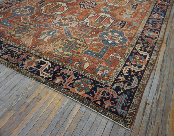 Terracotta and navy blue rug with stylized motifs rests on gray and yellow weathered plank flooring.