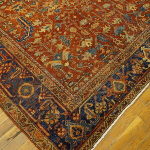 Intricate low-pile rug featuring a rust field and a dark navy border rests on bright wood planks.