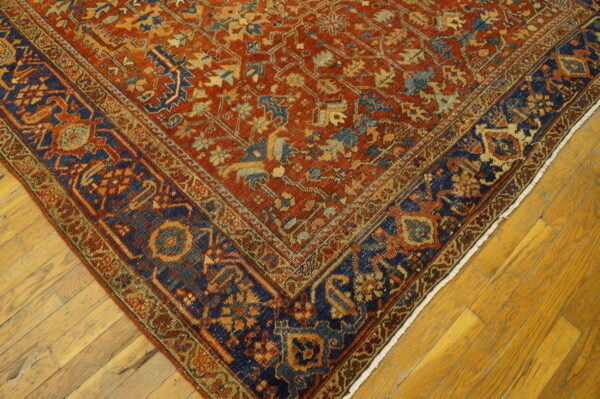Intricate low-pile rug featuring a rust field and a dark navy border rests on bright wood planks.