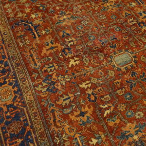 Closeup of a traditional rust and navy rug with detailed geometric and floral motifs on wood floor.