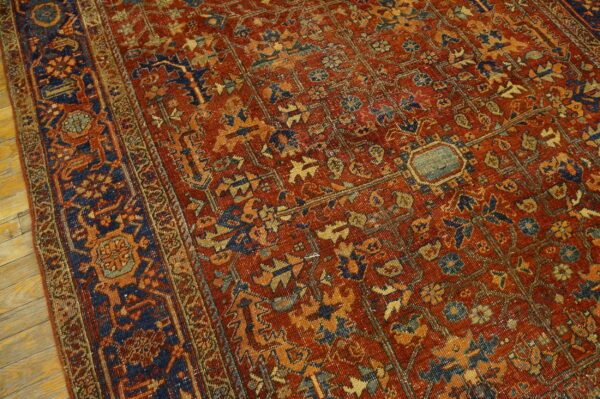 Closeup of a traditional rust and navy rug with detailed geometric and floral motifs on wood floor.