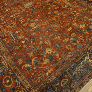 Ornate traditional low-pile rug in deep red, navy, and gold on light brown wood flooring.