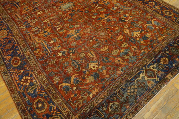 Ornate traditional low-pile rug in deep red, navy, and gold on light brown wood flooring.