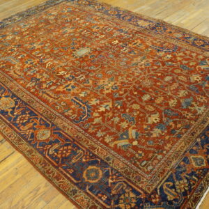 Rust and navy blue low-pile rug with intricate traditional patterns rests on aged hardwood floors.