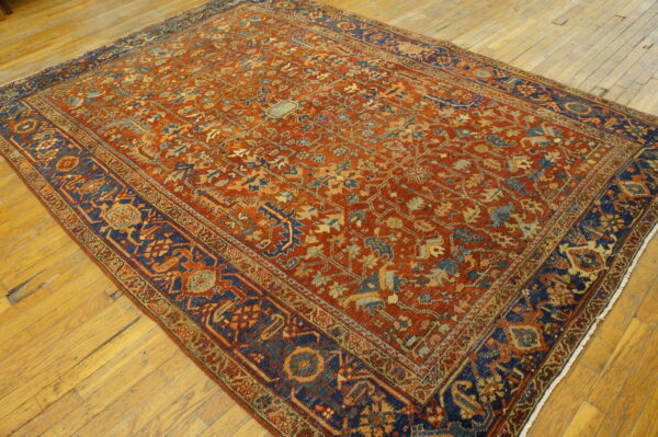 Rust and navy blue low-pile rug with intricate traditional patterns rests on aged hardwood floors.