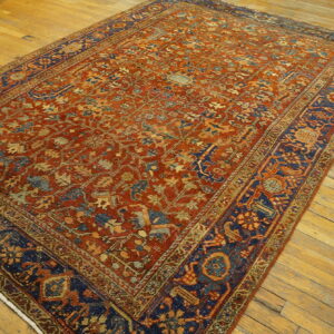 Terracotta rug with an intricate pattern and dark blue border lies on light wooden plank flooring.