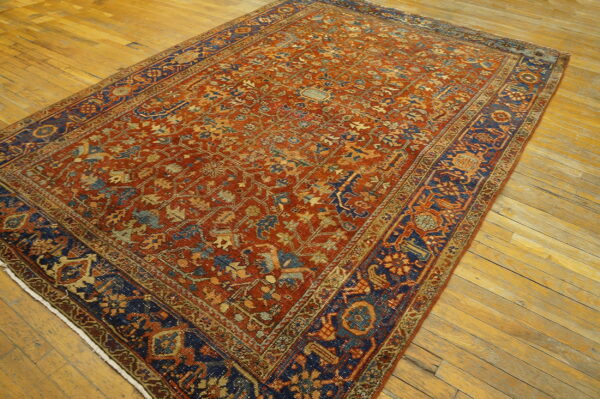 Terracotta rug with an intricate pattern and dark blue border lies on light wooden plank flooring.