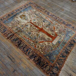 Cream, orange, and blue rug with a central Tree of Life design on distressed gray wood flooring.