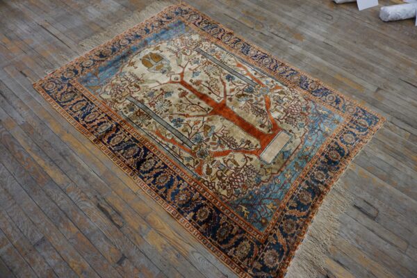 Cream, orange, and blue rug with a central tree of life design on distressed gray wood flooring.