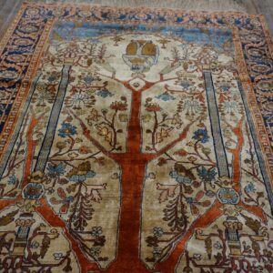 Cream and orange rug featuring a Tree of Life design and blue border on distressed wood flooring.