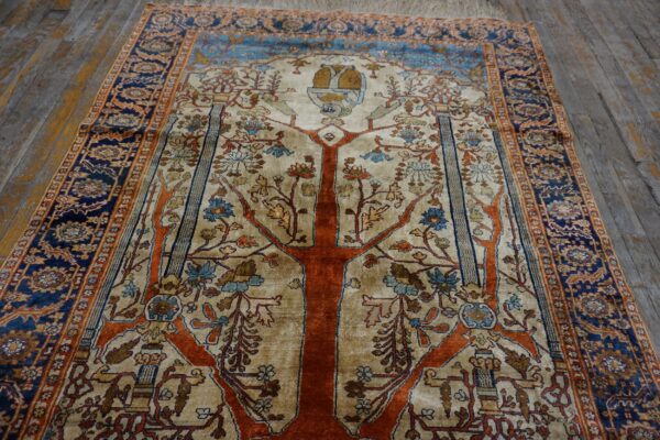 Cream and orange rug featuring a tree of life design and blue border on distressed wood flooring.