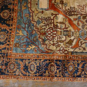 Ornate rug corner showing beige, deep blue, and terracotta floral patterns on distressed wooden floorboards.