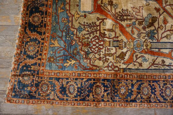 Ornate rug corner showing beige, deep blue, and terracotta floral patterns on distressed wooden floorboards.