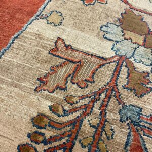 Beige rug detail featuring stylized foliage in rust, blue, and brown next to a solid orange border section.