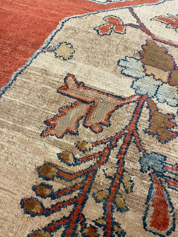 Beige rug detail featuring stylized foliage in rust, blue, and brown next to a solid orange border section.