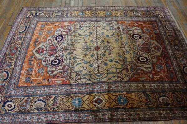 Beige medallion rug with terracotta and blue floral designs lying on rustic hardwood floor.