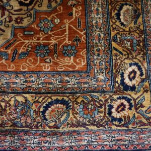 Detailed rust and gold floral rug corner rests on glossy brown hardwood plank flooring.