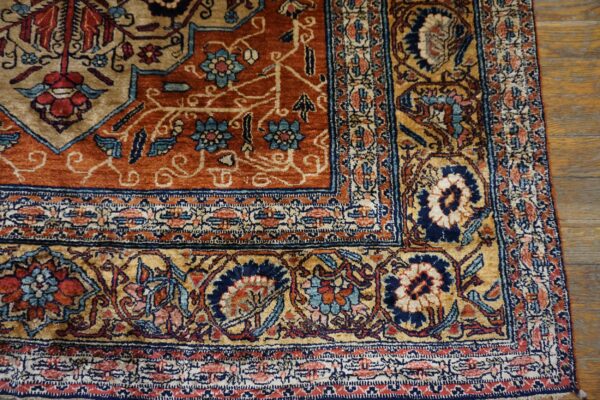 Detailed rust and gold floral rug corner rests on glossy brown hardwood plank flooring.