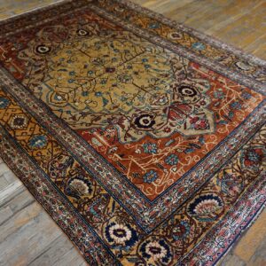 Traditional rug in gold, rust, and navy floral patterns rests on weathered wood plank flooring.